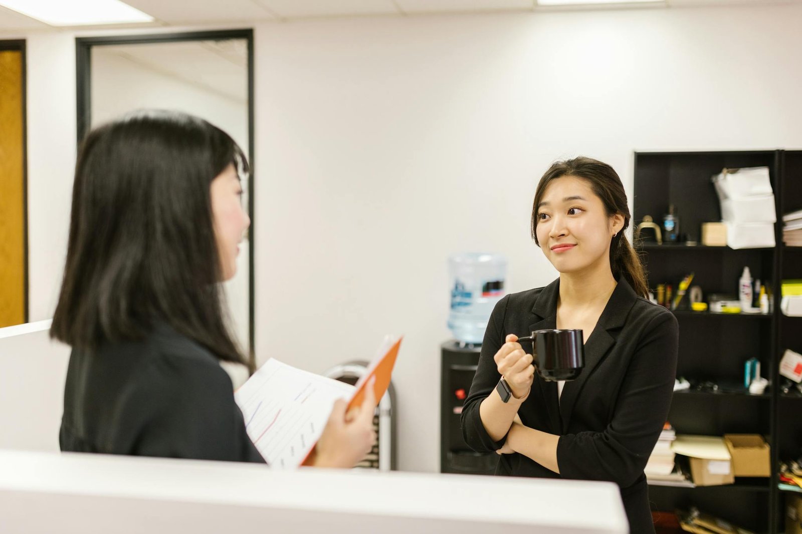 A Woman Listening to a Coworker while Holding a Mug at an Office